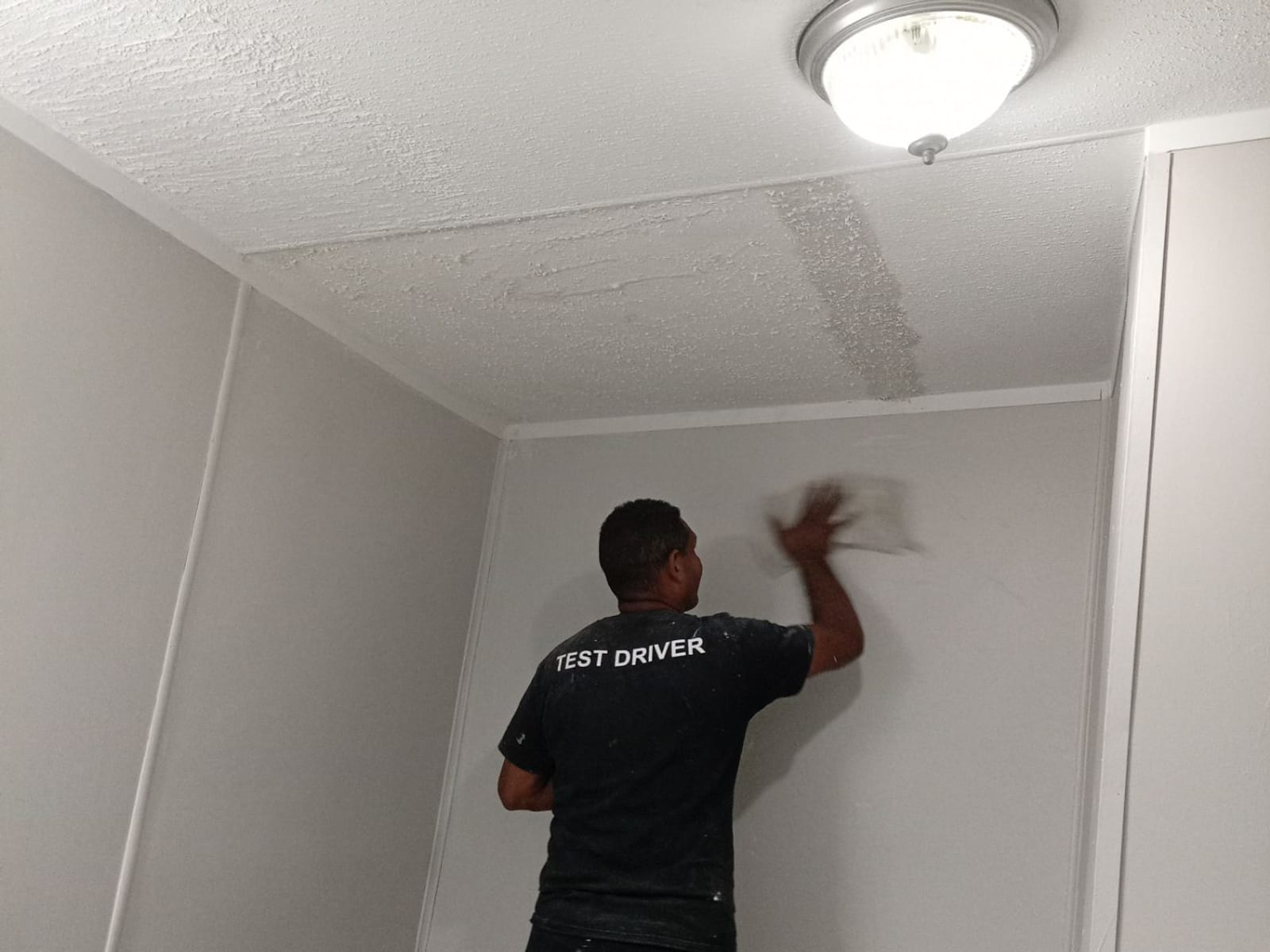 A crew member finishing the repaired ceiling with a taping knife.