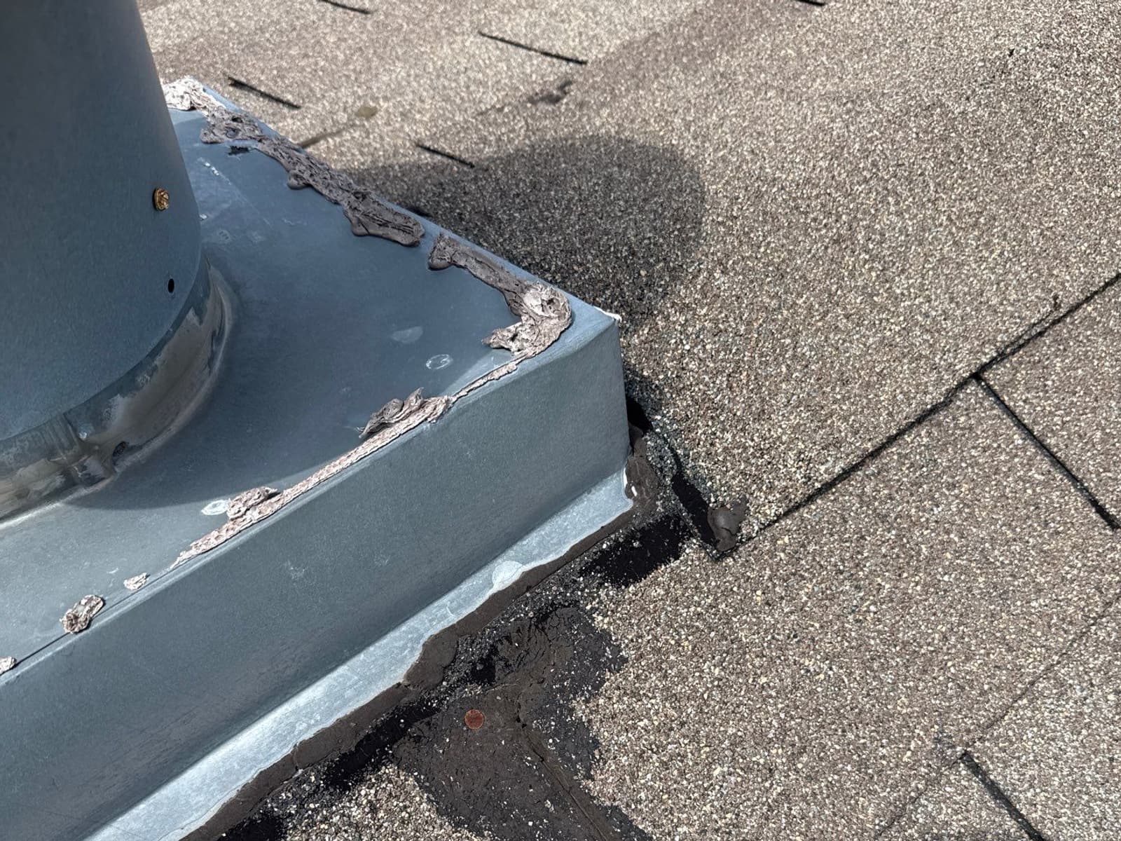 A failed vent flashing on a mobile home roof: cracked sealant and a torn shingle beside it.