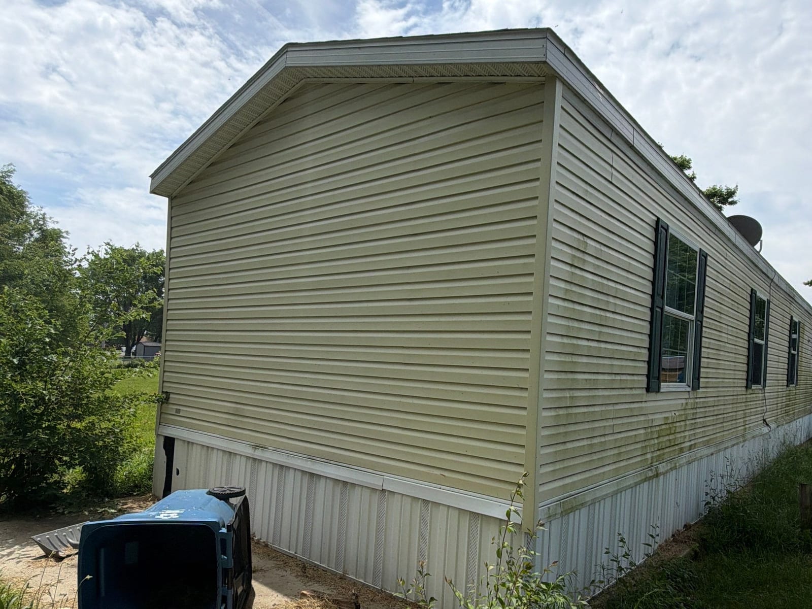 Before: a cream single-wide with heavy green algae streaking down the siding and dented skirting.