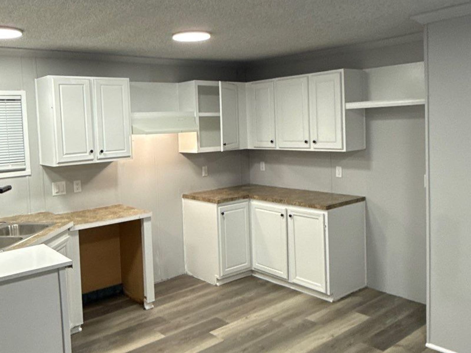 After: the same corner in white shaker cabinets with new counters and new plank flooring.