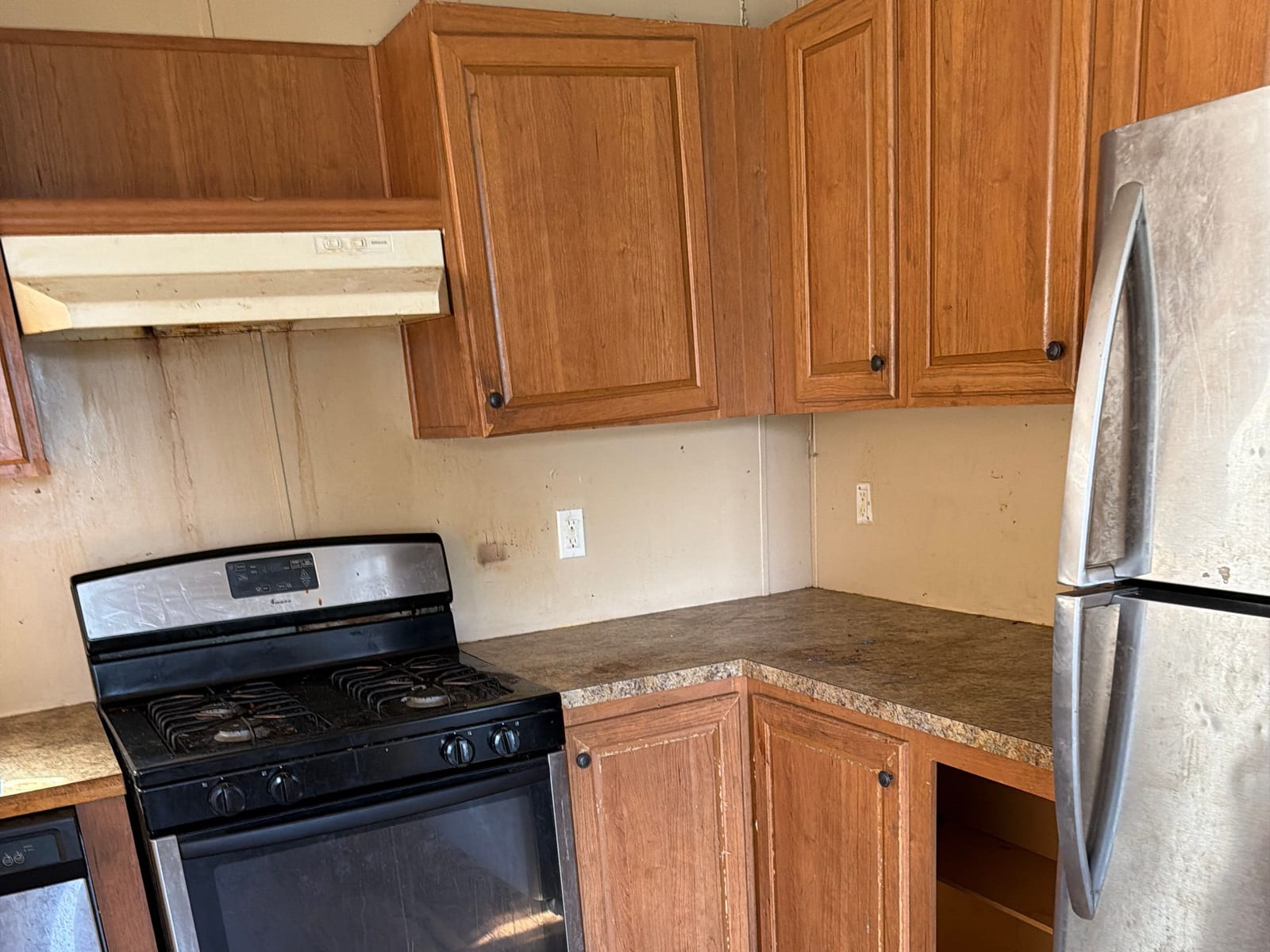 Before: dated oak kitchen cabinets over a worn laminate counter and water-damaged flooring.